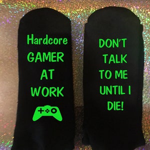 以下が含まれることがあります： 「Hardcore GAMER AT WORK」と「DON'T TALK TO ME UNTIL I DIE！」というネオングリーンの文字が書かれた黒い靴下。ネオングリーンのゲームコントローラーのグラフィックも付いています。