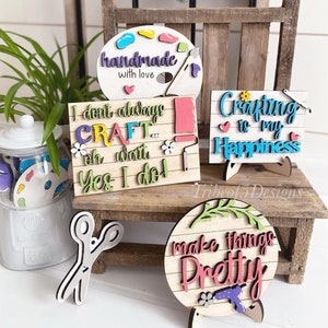 May include: A set of five wooden signs with colourful painted lettering and designs. The signs feature the words "Create", "Handmade with love", "I don't always craft...oh wait, yes I do!", "Crafting is my happiness", and "Make things pretty".