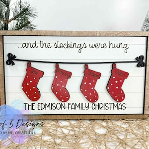 May include: Wooden Christmas sign with the text "...and the stockings were hung" and "THE EDMISON FAMILY CHRISTMAS". It features four red stockings with white polka dots, each with a name. The sign is in a wooden frame.