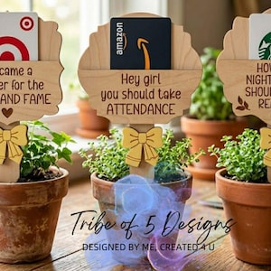 Puede incluir: Tres peque&ntilde;as plantas en macetas con letreros de madera. Cada letrero contiene una tarjeta de regalo y un mensaje diferente: "I became a teacher for the MONEY AND FAME", "Hey girl you should take ATTENDANCE", y "HOW MANY NIGHTS A WEEK SHOULD YOU BE READING? 6-7".
