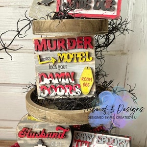 May include: A tiered tray decorated with Halloween-themed signs. The top sign reads "Hello, My Name Is Jane Doe". The middle sign reads "Murder Motel, Vacancy, Lock Your Damn Doors, Room 666". The bottom tier has two signs, one that reads "The Husband Did It" and the other that reads "Stay Spooky and Don't Get Murdered".