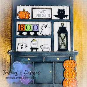 May include: A navy blue Halloween-themed cabinet decoration with orange pumpkins, a black bat, and the text "HAPPY HALLOWEEN." The cabinet has the word "BOO" in colorful blocks, a ghost, and a lantern. The bottom has a stack of pumpkins.