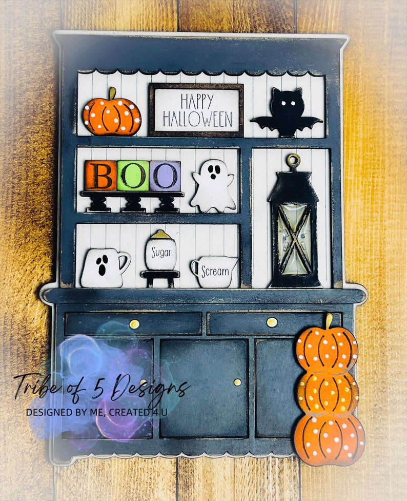 May include: A navy blue Halloween-themed cabinet decoration with orange pumpkins, a black bat, and the text "HAPPY HALLOWEEN." The cabinet has the word "BOO" in colorful blocks, a ghost, and a lantern. The bottom has a stack of pumpkins.