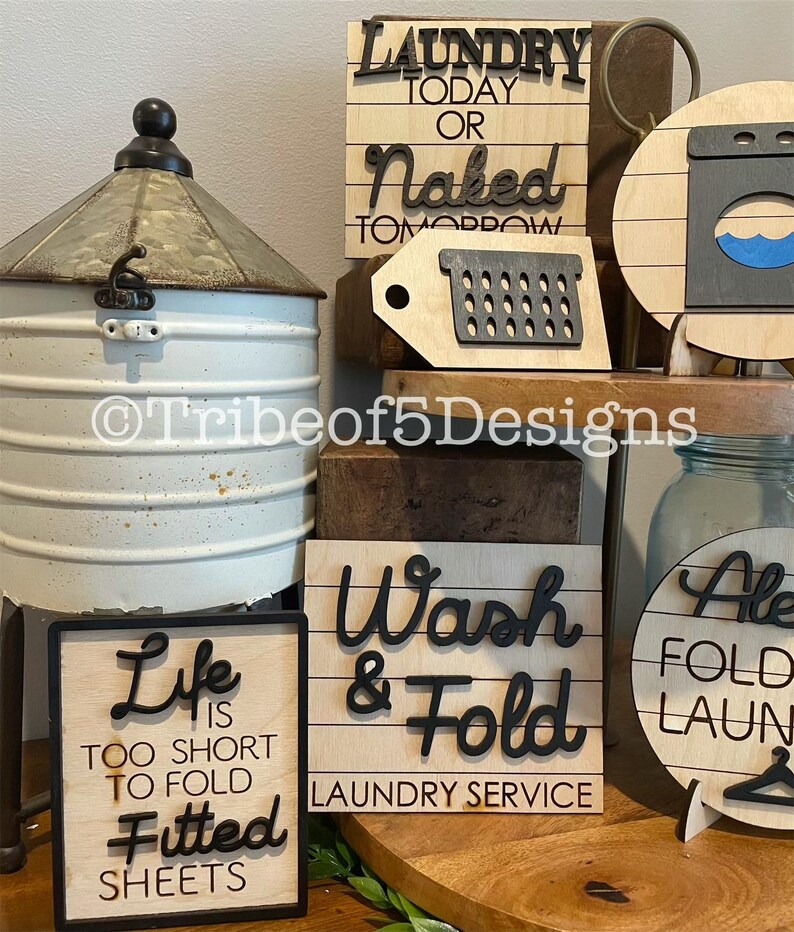 May include: A selection of wooden laundry signs with black lettering. One sign says "Laundry Today or Naked Tomorrow." Another reads "Wash & Fold Laundry Service." A third sign states "Life is too short to fold fitted sheets."