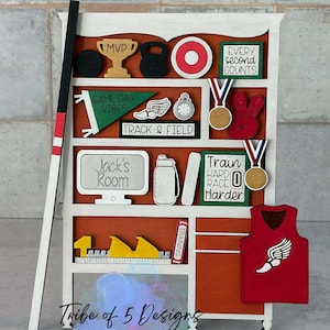 May include: A wooden shelf with sports-themed decorations. Includes a trophy, kettlebell, target, medals, and track and field elements. The shelf is white with an orange backing and features the text "Jack's Room".