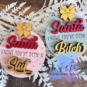 May include: Two round Christmas ornaments with a wooden bow at the top. One is pink with the text "Santa Knows You've Been A Slut" and the other is blue with "Santa Knows You've Been A Bitch".