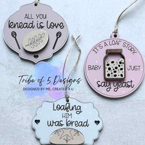 May include: Three decorative wooden ornaments with pun-based phrases related to baking. One ornament says "All you knead is love", another says "It's a loaf story, baby, just say yeast", and the third says "Loafing him was bread". Each ornament has a string for hanging.