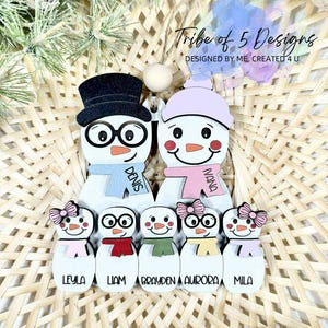 May include: A wooden family ornament featuring snowmen with names. The top snowmen wear a black top hat and a light purple hat. The ornament includes the text "Tribe of 5 Designs" and the names: Denis, Ivana, Leyla, Liam, Brayden, Aurora, and Mila.