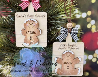May include: Wooden Christmas ornaments shaped like cutting boards, each featuring a gingerbread person and a festive bow. One reads "Santa's Sweet Sidekick" with the name "Kailyn", and the other says "Sticky Fingers, Sweeter Memories" with the name "Jacob".