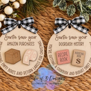 May include: Two round wooden ornaments with black and white buffalo check bows. The left ornament reads Santa saw your Amazon purchases, you're getting empty boxes and return labels for Christmas. The right reads Santa saw your Doordash history, you're getting a cookbook and budget sheet for Christmas.
