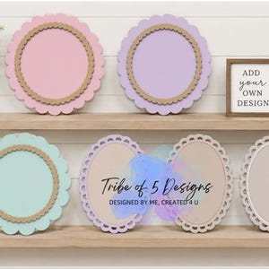 May include: A display of decorative wall art in pastel colors, including pink, purple, and teal, with scalloped edges and a natural wood-tone inner frame. The art pieces are arranged on wooden shelves with small potted plants and a sign that says "ADD your OWN DESIGN".