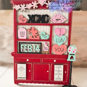May include: A red wooden hutch with a black sign that says "XOXO" and a variety of Valentine's Day themed decorations, including hearts, a cupid, and a love potion bottle. The hutch has two drawers and a sign that says "LOVE makes a HOUSE a HOME".