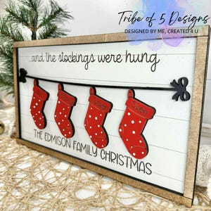 May include: Wooden framed Christmas sign with a white background and the text "...and the stockings were hung." Four red stockings with white polka dots are displayed, each with a name. The sign reads "THE EDMISON FAMILY CHRISTMAS."