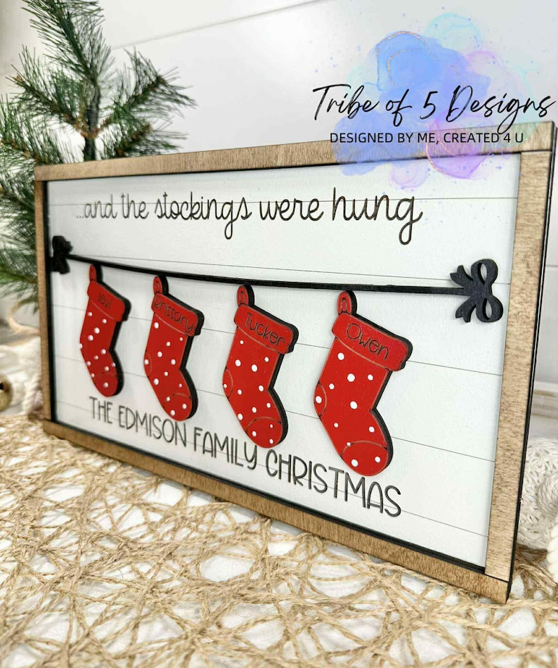 May include: Wooden framed Christmas sign with a white background and the text "...and the stockings were hung." Four red stockings with white polka dots are displayed, each with a name. The sign reads "THE EDMISON FAMILY CHRISTMAS."