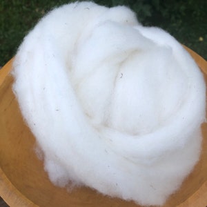 May include: A large amount of white wool fiber in a wooden bowl. The wool is soft and fluffy, and it is perfect for spinning or felting.