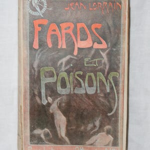 May include: A vintage book cover with a dark background and a title in red and green lettering that reads "Fards et Poisons" by Jean Lorrain. The cover features a stylized image of a woman in a flowing dress.