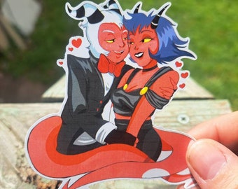 May include: A sticker featuring a red and white demon with horns and a black tuxedo holding a red and blue demon with horns and a black dress. The demons are smiling and have hearts around them.