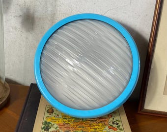May include: A round, light fixture with a bright blue frame. The center is a white, textured surface. The fixture is resting on a vintage map.