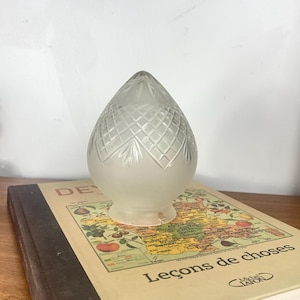 May include: A teardrop-shaped glass lamp shade featuring a frosted lower section and a clear, cut-glass diamond pattern on the upper portion. The shade has a circular opening at the base and a pointed top, showcasing intricate geometric detailing.