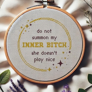 May include: A cross-stitch embroidery hoop with the text "do not summon my INNER BITCH. she doesn't play nice." The embroidery is surrounded by a wooden hoop, a white cloth, and sprigs of lavender, greenery, and a sunflower. The words "CROSS-STITCH PDF PATTERN" are at the bottom.