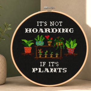Op de afbeelding: Een ronde houten borduurring met zwarte stof en een kruissteekpatroon van diverse potplanten op planken. De witte tekst luidt IT'S NOT HOARDING IF IT'S PLANTS. Het ontwerp bevat groene, rode en oranje garenkleuren.
