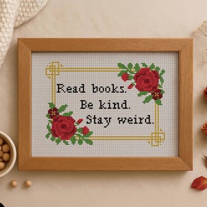 Könnte beinhalten: Gerahmtes Kreuzstichbild mit dem Text "Read books. Be kind. Stay weird." umgeben von roten Rosen und grünen Blättern. Der Rahmen ist hellbraun. Das Kreuzstichmuster ist 17,78 cm x 12,7 cm groß.
