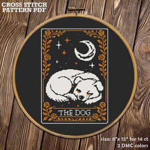 May include: Cross-stitch pattern PDF featuring a sleeping dog design. The image includes the text "THE DOG" and "size: 8" x 12" for 14 ct". The design is framed in a wooden hoop, with a black background and orange and white accents.