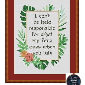 May include: Cross-stitch art framed in a brown wooden frame. The cross-stitch features the text "I can't be held responsible for what my face does when you talk" surrounded by green leaves and a pink flower. A small circular logo is in the bottom right corner.