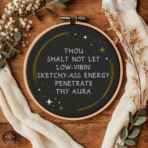 Puede incluir: Un bastidor de bordado de punto de cruz negro con el texto "THOU SHALT NOT LET LOW-VIBIN' SKETCHY-ASS ENERGY PENETRATE THY AURA" en blanco. El diseño incluye detalles dorados y estrellas. Las palabras están centradas.