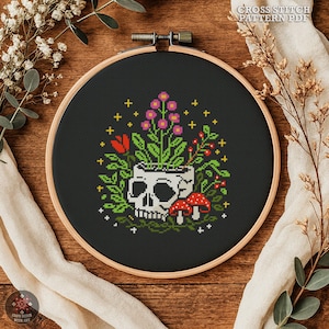 Könnte beinhalten: Ein Kreuzstichmuster in einem Holzrahmen zeigt einen Totenkopf-Pflanztopf mit bunten Blumen, roten Beeren und Pilzen auf schwarzem Hintergrund. Der Text "CROSS STITCH PATTERN PDF" ist sichtbar. Das Design ist von Grün umgeben.