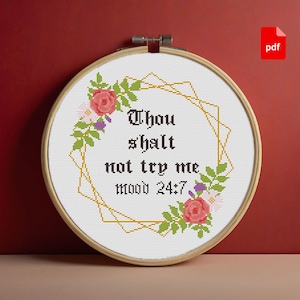 Op de afbeelding: Een witte borduurring met een gouden geometrisch frame en bloemmotieven. De tekst "Thou shalt not try me mood 24/7" is in zwart geborduurd.