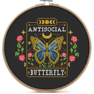 May include: A black embroidery hoop with a cross-stitch design of a butterfly with the text "Antisocial Butterfly" in yellow.