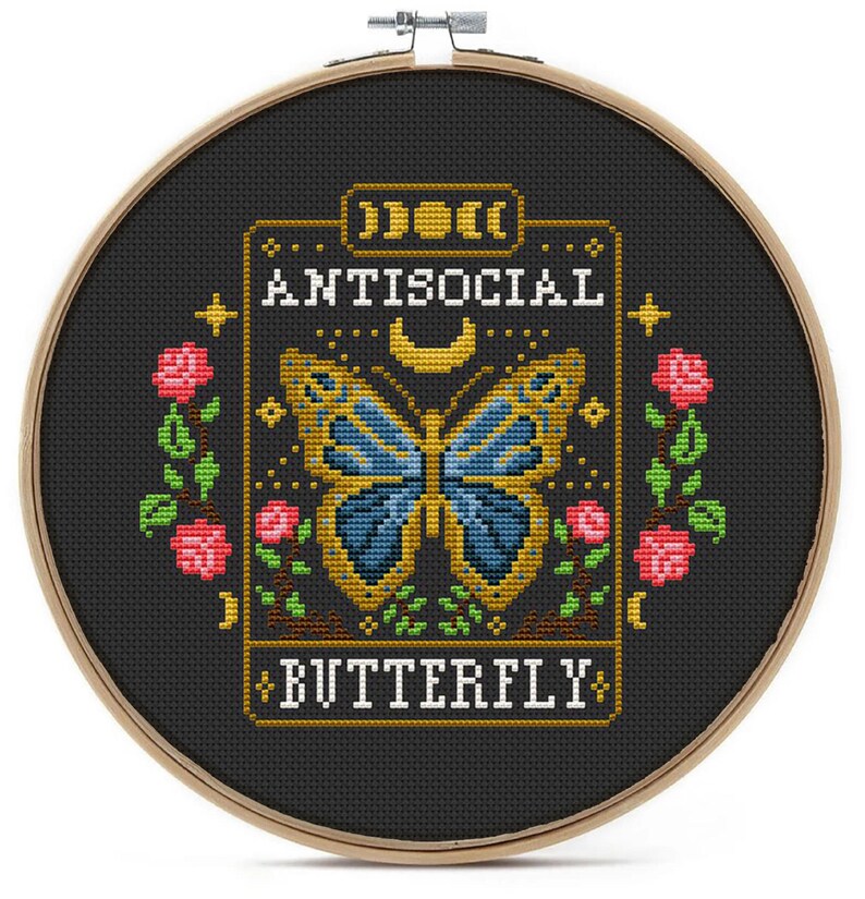 May include: A black embroidery hoop with a cross-stitch design of a butterfly with the text "Antisocial Butterfly" in yellow.