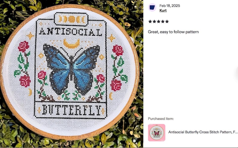 K&ouml;nnte beinhalten: Kreuzstich-Stickerei in einem Holzreifen. Das Design zeigt einen blauen Schmetterling mit den Worten "ANTISOCIAL BUTTERFLY" in schwarzem Text. Rote Rosen und gr&uuml;ne Bl&auml;tter umgeben den Schmetterling. Der Hintergrund ist eine gr&uuml;ne, belaubte Pflanze.