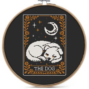 May include: A cross-stitch embroidery hoop featuring a black background with a white dog illustration. The design includes a crescent moon, stars, and the text "THE DOG" in a decorative frame. The hoop is made of wood.