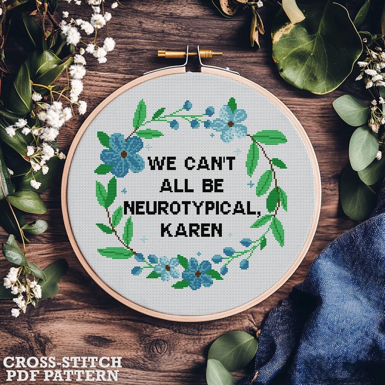 May include: A cross-stitch embroidery hoop with the text "WE CAN'T ALL BE NEUROTYPICAL, KAREN" surrounded by a floral wreath. The design features blue flowers and green leaves. The words "CROSS-STITCH PDF PATTERN" are at the bottom.