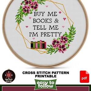 Cross-stitch pattern in a wooden hoop. The design features the text "BUY ME BOOKS & TELL ME I'M PRETTY" surrounded by floral and geometric elements. The design size is 10" x 10".