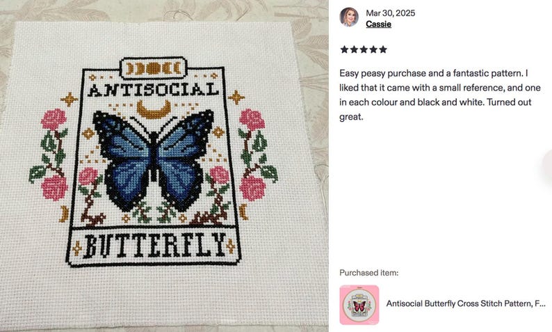 K&ouml;nnte beinhalten: Kreuzstichmuster mit einem blauen Schmetterling und dem Text "ANTISOCIAL BUTTERFLY". Das Design umfasst rosa Rosen und einen Mond. Das Muster befindet sich auf wei&szlig;em Stoff.