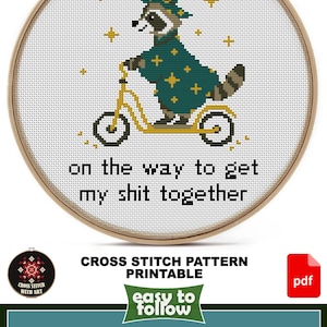 May include: Cross-stitch pattern featuring a raccoon riding a scooter, wearing a wizard hat and robe. The text reads "on the way to get my shit together." The design size is 6 1/2" x 7 1/2" for AIDA 14ct, with 6 DMC colors.