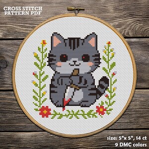 Op de afbeelding: Kruissteekpatroon PDF met een grijze kat met een mes, omringd door bloemmotieven. De kat heeft rode ogen en roze wangen. Het ontwerp is omlijst in een houten hoepel. De tekst "CROSS STITCH PATTERN PDF" staat bovenaan.