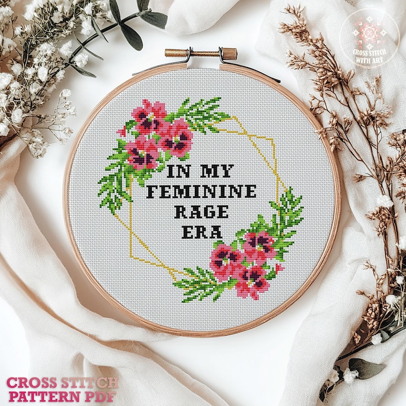 A cross stitch pattern featuring a floral wreath with pink flowers and green leaves. The wreath surrounds the text "In My Feminine Rage Era".
Cross stitch pattern featuring a floral design with the text "In My Feminine Rage Era". The pattern is 8 inches by 8 inches and is designed for 14 count Aida cloth. It uses 8 DMC colors and includes high quality charts in PDF and JPEG formats.