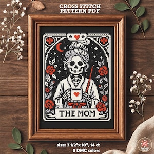 Cross-stitch pattern PDF featuring a skeletal figure holding a mug with a heart, surrounded by roses and stars. The design is framed in a wooden hoop, with the text "THE MOM" at the bottom. The pattern measures 7.5" x 10".
