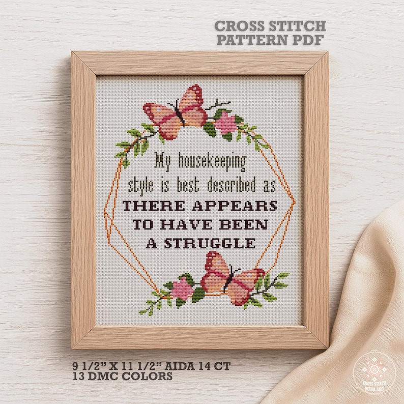 A cross stitch pattern featuring a quote about housekeeping, "My housekeeping style is best described as there appears to have been a struggle." The pattern includes butterflies, flowers, and a geometric frame. The pattern is 9.5 inches by 11.5 inches and uses 13 DMC colors.