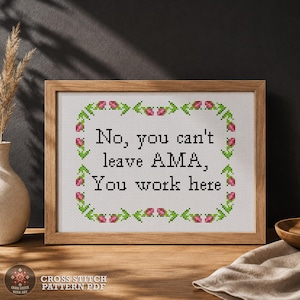 May include: A framed cross-stitch piece featuring the black text No, you can't leave AMA, You work here, surrounded by a rectangular border of small pink tulips with green stems and leaves, all set against a white fabric background.
