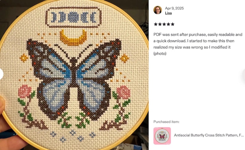 K&ouml;nnte beinhalten: Fertige Kreuzstichstickerei in einem Holzrahmen. Das Design zeigt einen blauen Schmetterling, einen Mond und Mondphasen. Rosa Blumen und Sterne umgeben den Schmetterling. Der Text "Antisocial Butterfly Cross Stitch Pattern" ist sichtbar.