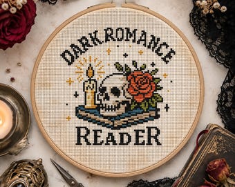 May include: A circular wooden embroidery hoop containing a cross-stitch design on cream fabric. The design features a skull, a red rose, and a lit candle resting on a book, with the black text "DARK ROMANCE READER" stitched above and below.