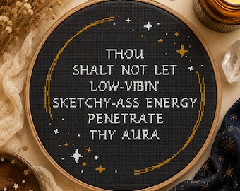 Könnte beinhalten: Ein runder hölzerner Stickrahmen mit schwarzem Stoff, der den in weißem Kreuzstich gestickten Text enthält: THOU SHALT NOT LET LOW-VIBIN' SKETCHY-ASS ENERGY PENETRATE THY AURA. Das Design zeigt einen goldenen Halbmond und kleine weiße und goldene Sterne.
