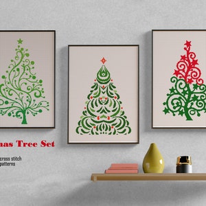 Puede incluir: Conjunto de tres patrones de punto de cruz enmarcados con árboles de Navidad estilizados en verde y rojo. El texto "Xmas Tree Set" se muestra debajo de los marcos. Una estantería con objetos decorativos está en primer plano.