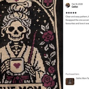 K&ouml;nnte beinhalten: Kreuzstichmuster mit einer Skelettfigur mit Krone, die eine Tasse mit einem Herzen h&auml;lt, und dem Text "THE MOM". Das Design umfasst Rosen, Sterne und einen Mond, alles im gotischen Stil. Die Farbpalette umfasst Schwarz, Creme und Burgunderrot.