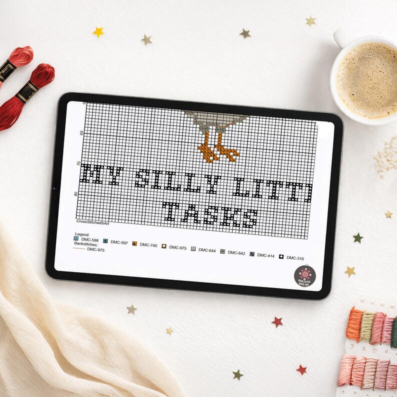 May include: A digital tablet displaying a cross-stitch pattern grid featuring the text "MY SILLY LITTI TASKS" in black, with orange bird feet visible above the text and a color legend at the bottom listing various DMC thread color codes.